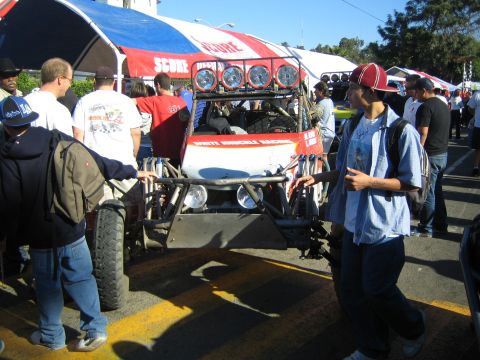 1990 Ford Bronco - open-bodied off-road race buggy with roof light pods sits at a SCORE event while spectators pass by on the pavement.