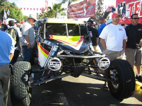 1990 Ford Bronco - open-wheel off-road race car with exposed tube chassis, Hella lights and visible suspension is shown to onlookers at an event.