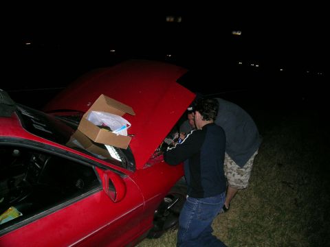 1993 Ford Probe - Two individuals are gathered around the open engine bay of a red car under the cover of darkness.