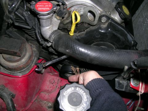 1993 Ford Probe - A hand turns the power steering fluid cap in a vehicle's engine bay, with a red fender and various engine components visible.
