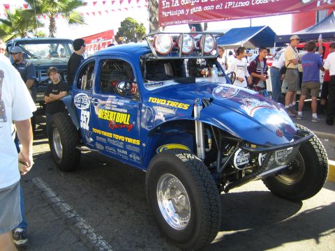 1990 Ford Bronco - blue Volkswagen-based Baja Bug race car with Desert Bull Racing and Toyo Tires graphics sits on display at an outdoor race event.