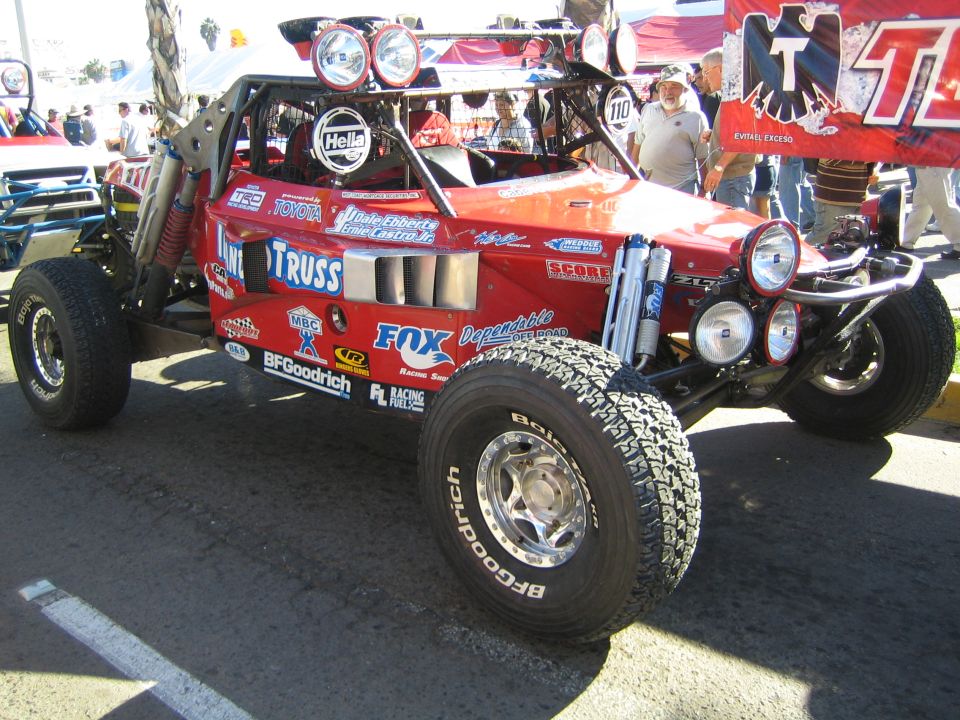 Red open-wheel off-road race buggy with Fox, BFGoodrich and Truss graphics and roof light bar on pavement