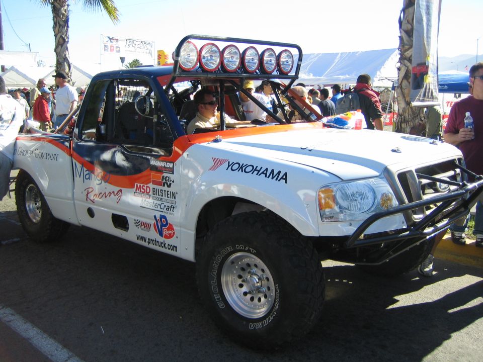 White off-road race truck with orange graphics, Yokohama branding and roof light bar, driver seated inside