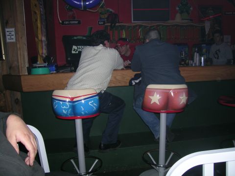 1993 Ford Probe - People are gathered at a bar, some seated on novelty stools shaped like buttocks.