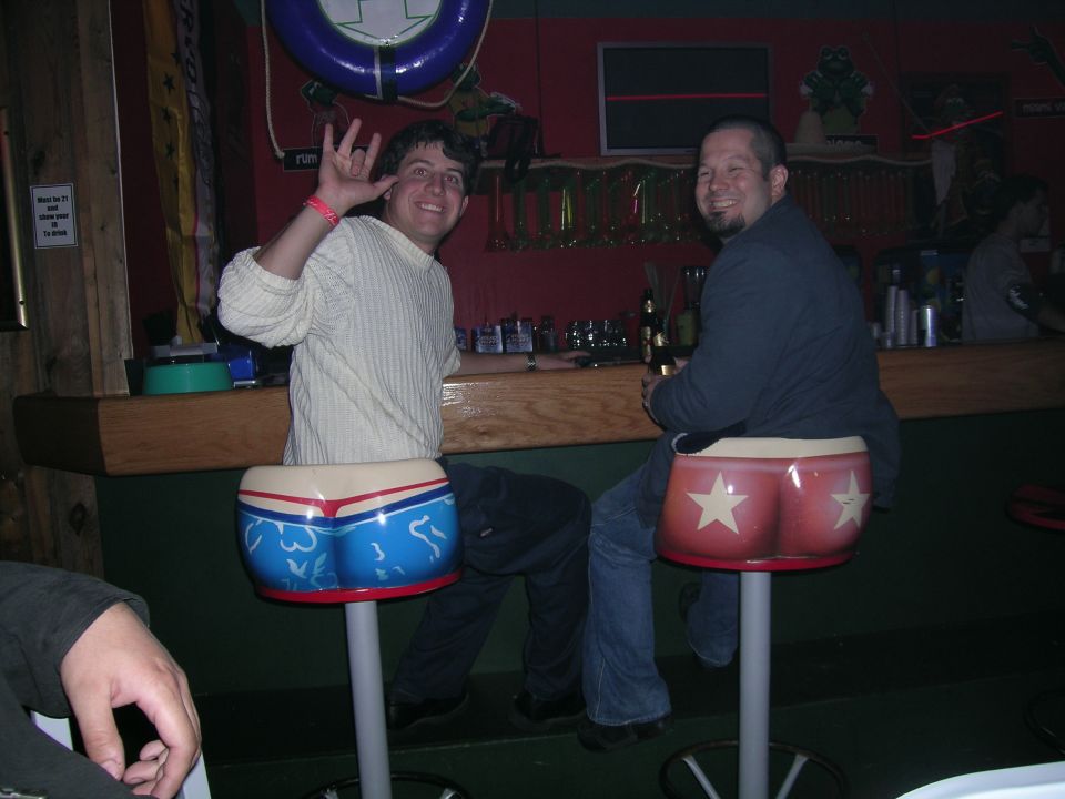 Two men sitting at a bar, one waving