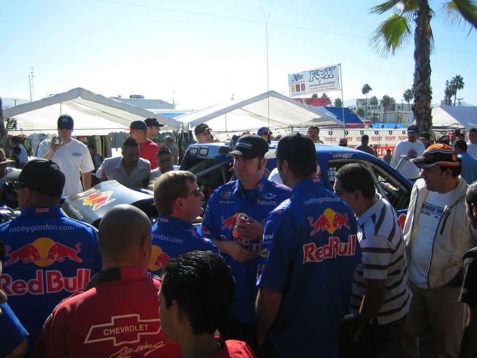 Crew in blue Red Bull racing shirts gather and talk near tents at an outdoor desert race event