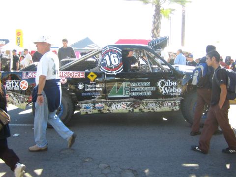 1990 Ford Bronco - black off-road race truck numbered 16 with McGraw Insurance and Cabo Wabo graphics sits at an event as people walk past.