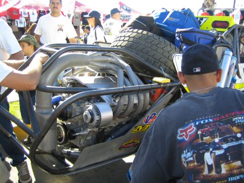 1990 Ford Bronco - Close-up of the exposed mid-mounted engine and tube chassis of an off-road race buggy with a spare tire mounted overhead.