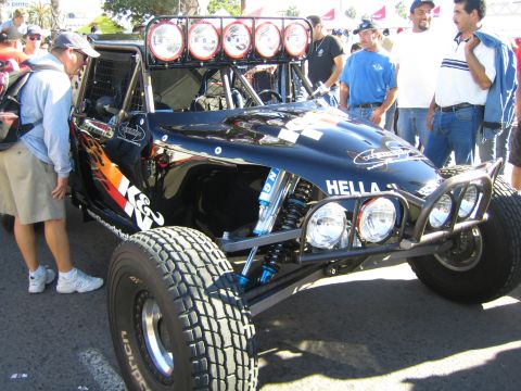 1990 Ford Bronco - black tube-frame off-road buggy with flame graphics and a five-pod light bar, surrounded by spectators at an event.