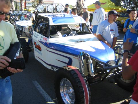 1990 Ford Bronco - blue and white tube-frame off-road buggy with a four-pod roof light bar, drawing a crowd at an outdoor event.