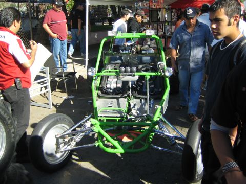 1990 Ford Bronco - bright green tube-frame off-road buggy with exposed engine and suspension, viewed head-on among spectators.