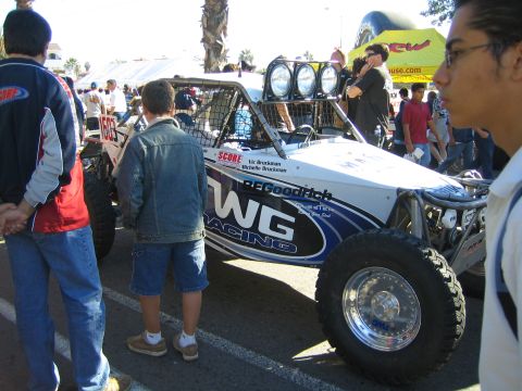 1990 Ford Bronco - white and blue tube-frame off-road buggy with WG Racing livery and a four-pod roof light bar, watched by onlookers.