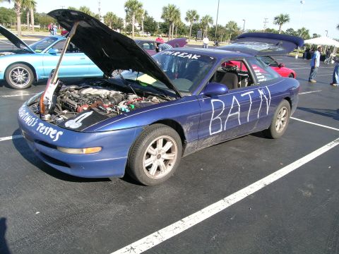 1993 Ford Probe - A blue coupe is parked with its hood open, revealing the engine and a guitar. The car has custom writing on its exterior.