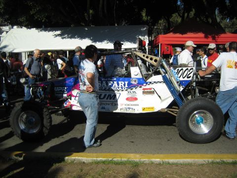 1990 Ford Bronco - blue and white long-travel off-road buggy, number 1002, with Safari livery, parked under tents at a racing event.