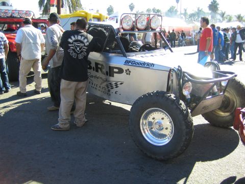 1990 Ford Bronco - silver tube-frame off-road buggy with BRP Racing livery and a four-pod roof light bar, surrounded by a crowd.