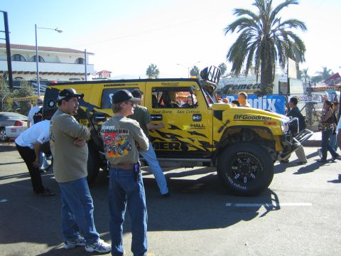 1990 Ford Bronco - yellow Hummer off-road race truck with tribal-flame graphics and HUMMER badging, watched by spectators under palms.