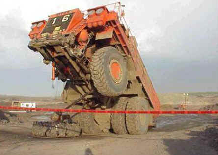 1991 Ford Bronco - A large mining dump truck has tipped over, with one of its massive tires lying detached on the ground.