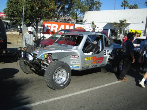 1990 Ford Bronco - silver and red off-road race truck, BC-13, with an exposed tube front bumper, parked on a street near a Fram sign.