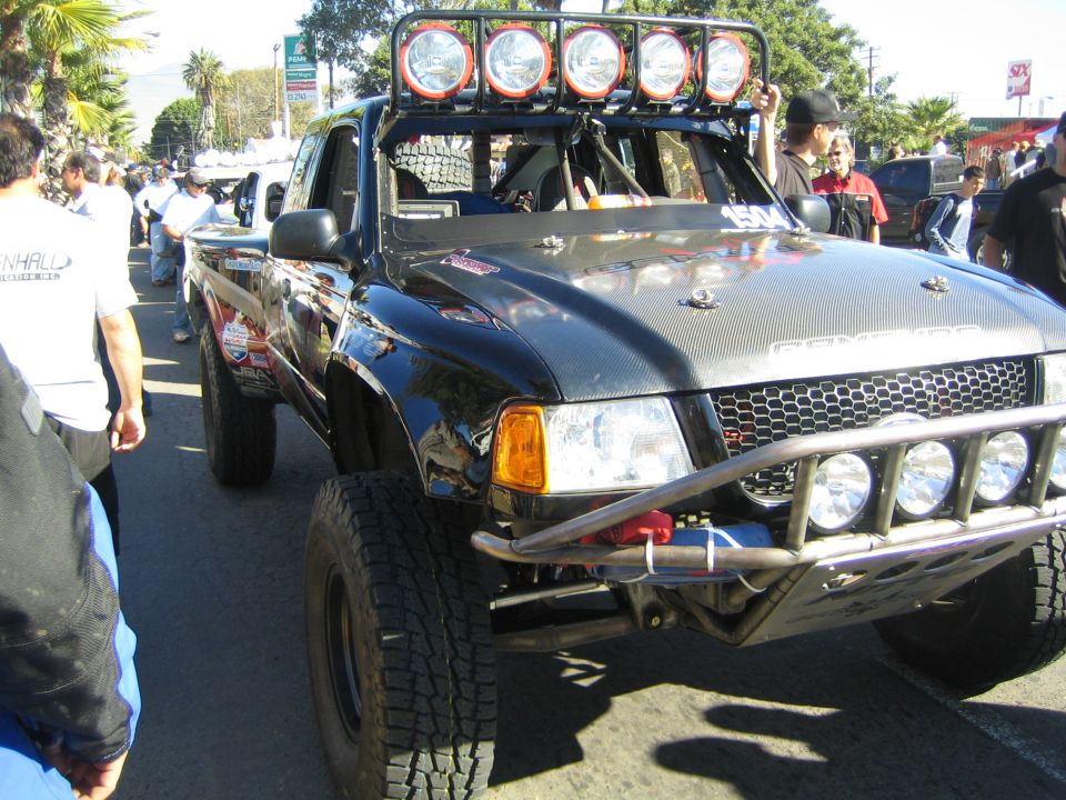 Black off-road race truck with five-light roof bar and tube bumper in a street