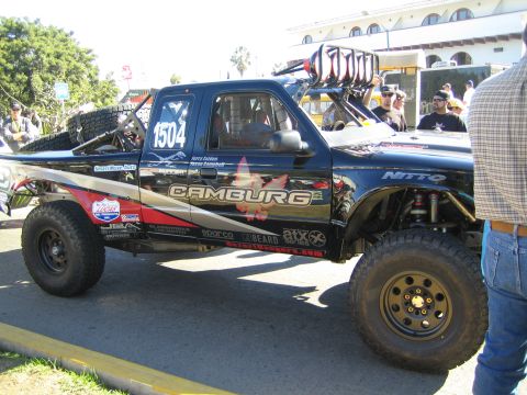 1990 Ford Bronco - black off-road race truck, number 1504, with Camburg livery and visible bypass shocks, parked among spectators.