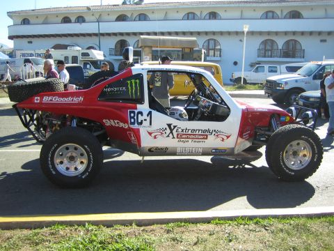 1990 Ford Bronco - red-and-white tube-frame desert race buggy marked BC-1 with Extremely Canadian Baja Team livery is parked on a street.
