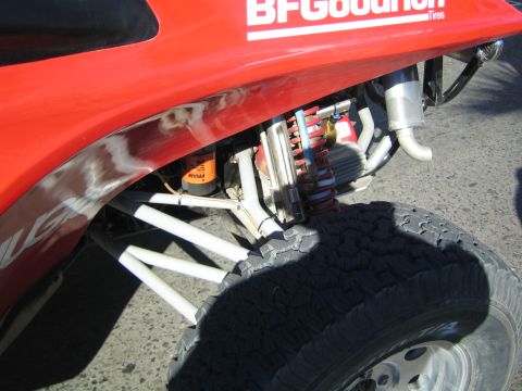 1990 Ford Bronco - close-up of the rear of a red off-road buggy showing exhaust pipe, suspension links, a tire and a BFGoodrich Tires fender decal.