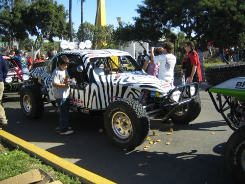 1990 Ford Bronco - white desert race buggy painted with black zebra stripes and PIAA lights sits in a street as a boy stands next to it.