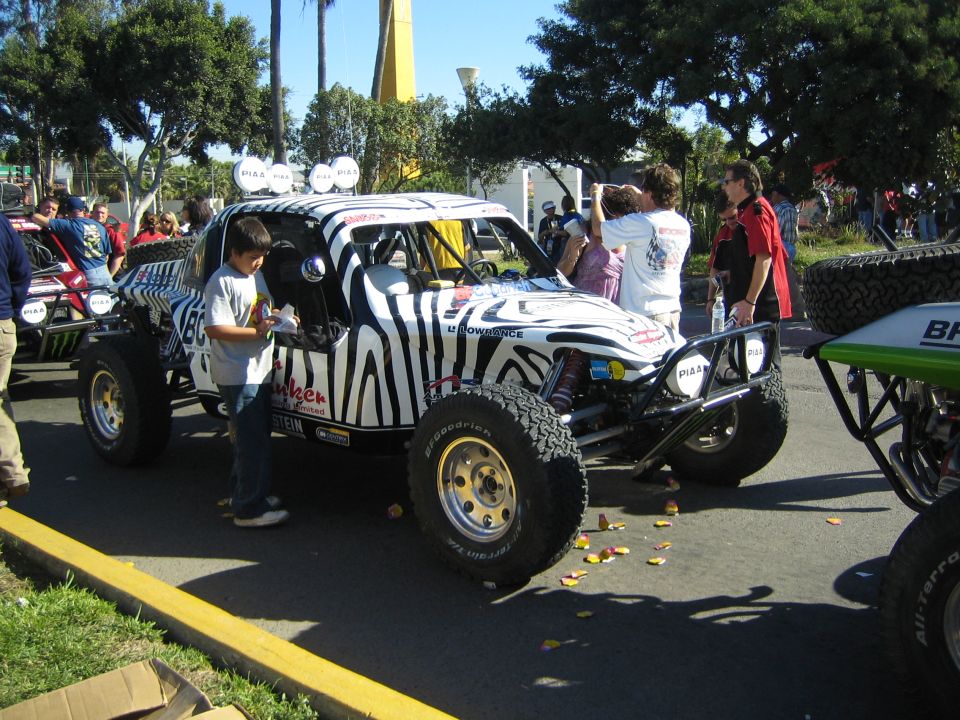 White and black zebra-striped desert race buggy with PIAA lights and a boy beside it