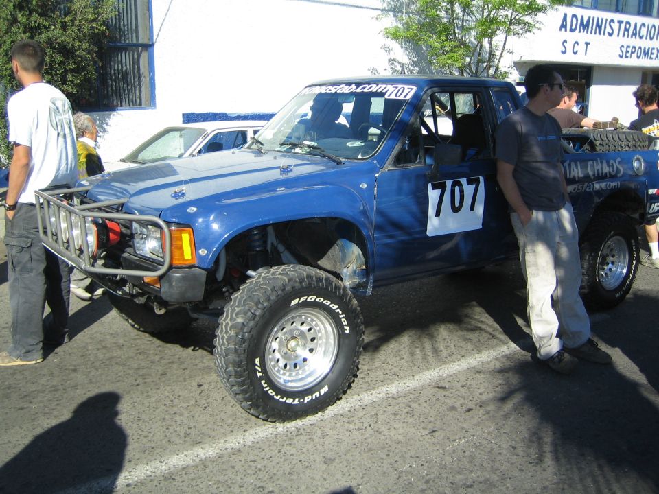 Blue lifted pickup race truck number 707 with brush guard and winch, people standing by