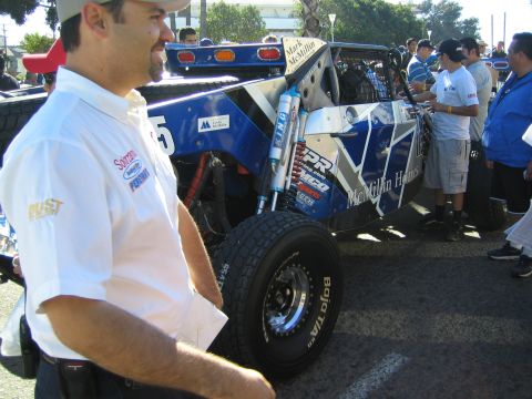 1990 Ford Bronco - blue-and-white McMillin Homes desert race buggy with King shocks is parked as a man in a white shirt stands in the foreground.
