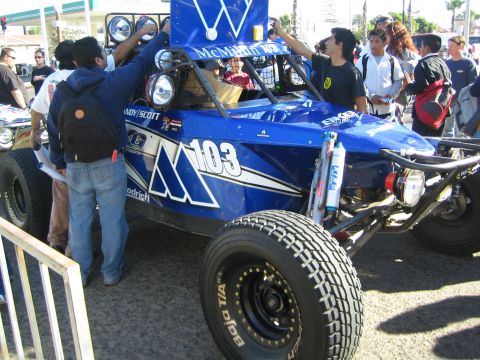 1990 Ford Bronco - blue tube-frame desert race buggy marked 103 with McMillin livery is crowded by spectators on Bajo T/A tires.