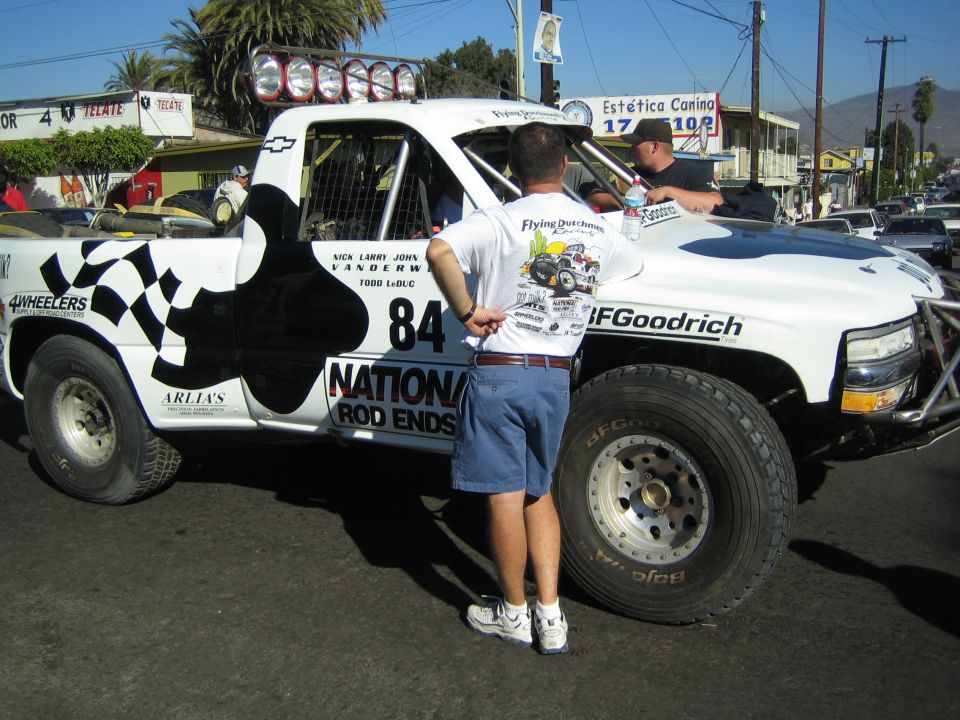 White Chevrolet race truck number 84 with checkered flag graphics, man in front