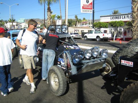 1990 Ford Bronco - gray tube-frame desert buggy with Fox shocks and a row of off-road lights sits on a street near a Tecate beer sign.