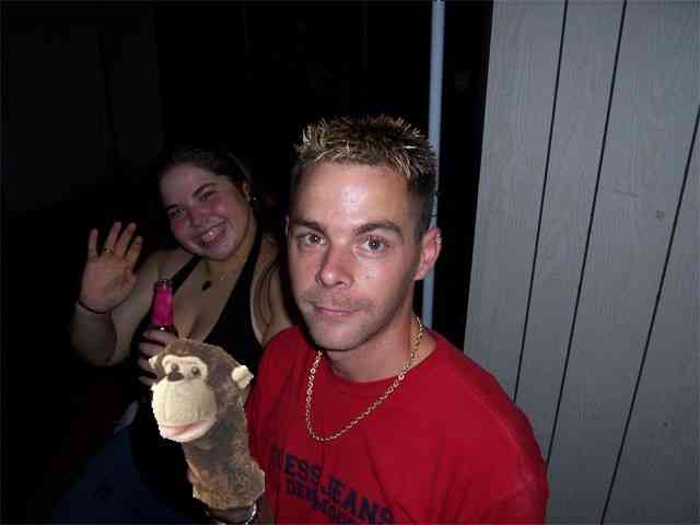 Woman waves while holding a pink bottle, man in red shirt holds monkey puppet