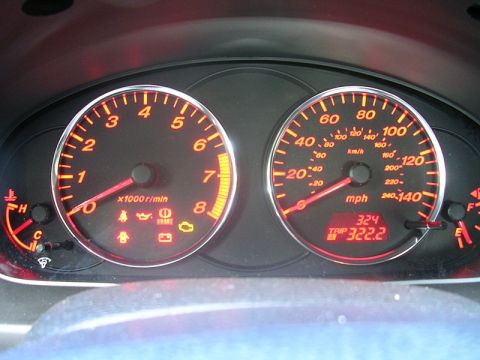 2004 Mazda 6 - The illuminated dashboard gauges display the vehicle's speed and engine RPM, with various warning lights illuminated.