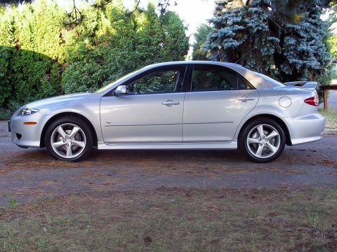 2004 Mazda 6 - Side profile of a silver sedan with a spoiler, parked outdoors with lush green trees behind it.