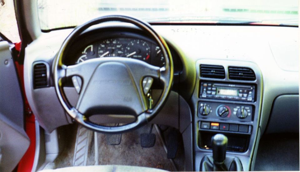 Dashboard of a 1996 Ford Probe, showing the steering wheel, instrument cluster, and center console with radio and climate controls
