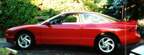 1996 Ford Probe - A red 1996 Ford Probe is shown from the side, parked in front of greenery.