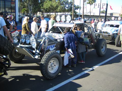 1990 Ford Bronco - black tube-frame race buggy with Fox decals and a bank of driving lights sits in a row of buggies amid a crowd.