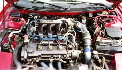 1996 Ford Probe - The engine bay of a red Mazda is visible with the hood open, showing the V6 engine and various components.