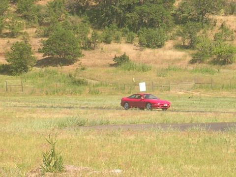 1996 Ford Probe - A red 1996 Ford Probe is parked on a dirt road with grassy hills behind it.