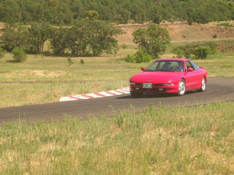 1996 Ford Probe - A red coupe drives on a racetrack with grassy hills in the background.