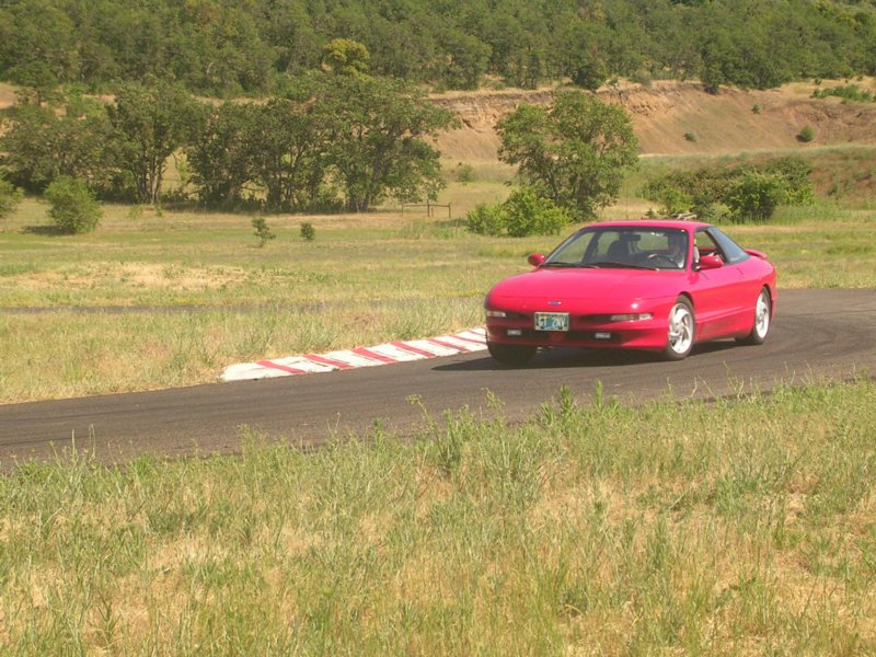 Red coupe on a racetrack, 3/4 front view. License plate is visible