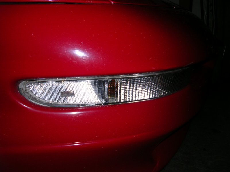 close-up of a red car's front corner with a clear turn signal lens