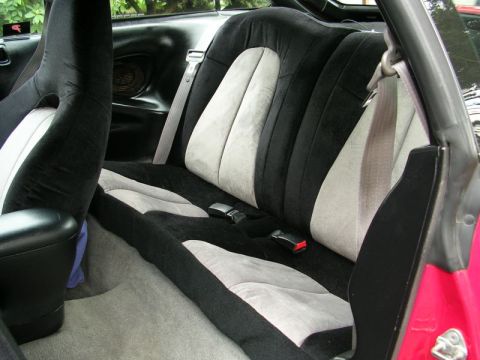 1996 Ford Probe - The rear interior of a car shows two-tone seats with visible seat belts and a black center console.