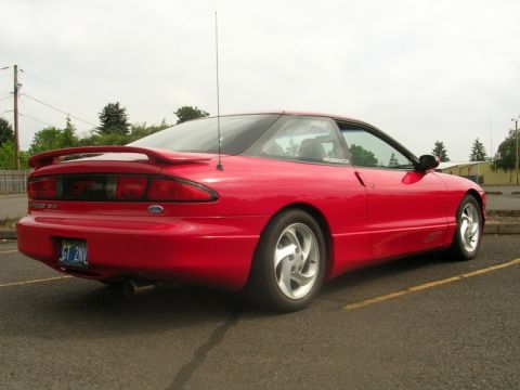 1996 Ford Probe - The rear of a red 1996 Ford Probe GT coupe is visible, parked in a lot with yellow lines.