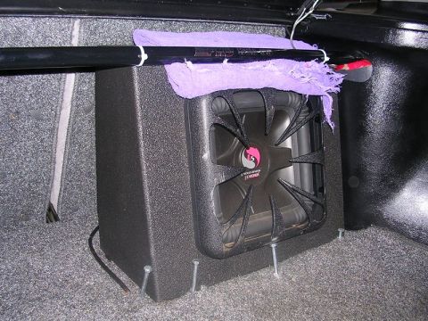 1996 Ford Probe - A Kicker subwoofer is installed in the trunk of a car, secured with screws to the carpeted floor.