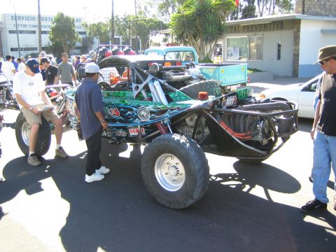 1990 Ford Bronco - green tube-frame off-road buggy with a visible rear engine and long-travel shocks sits on a street as bystanders gather around it.