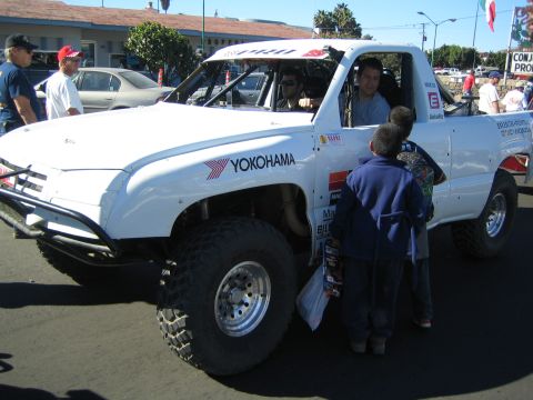 1990 Ford Bronco - white off-road race truck wearing Yokohama and sponsor decals with a roof number 6 sits curbside as children peer at the cab.