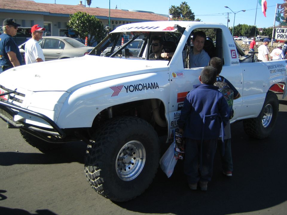 White off-road race truck with Yokohama decals and roof number 6, children looking on